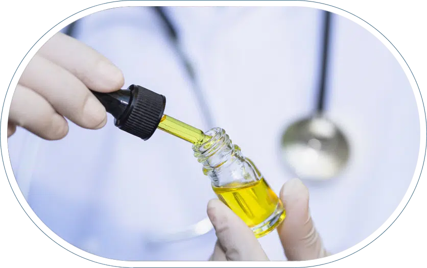 Hands wearing white latex gloved dropping CBD oil for pain management into a glass bottle.