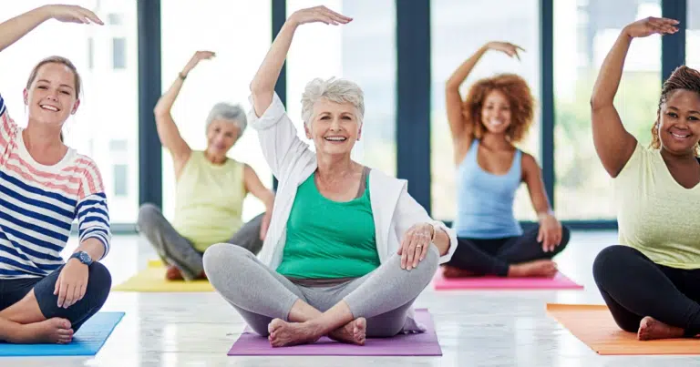 Diverse group of women smiling and stretching together in a bright community yoga class